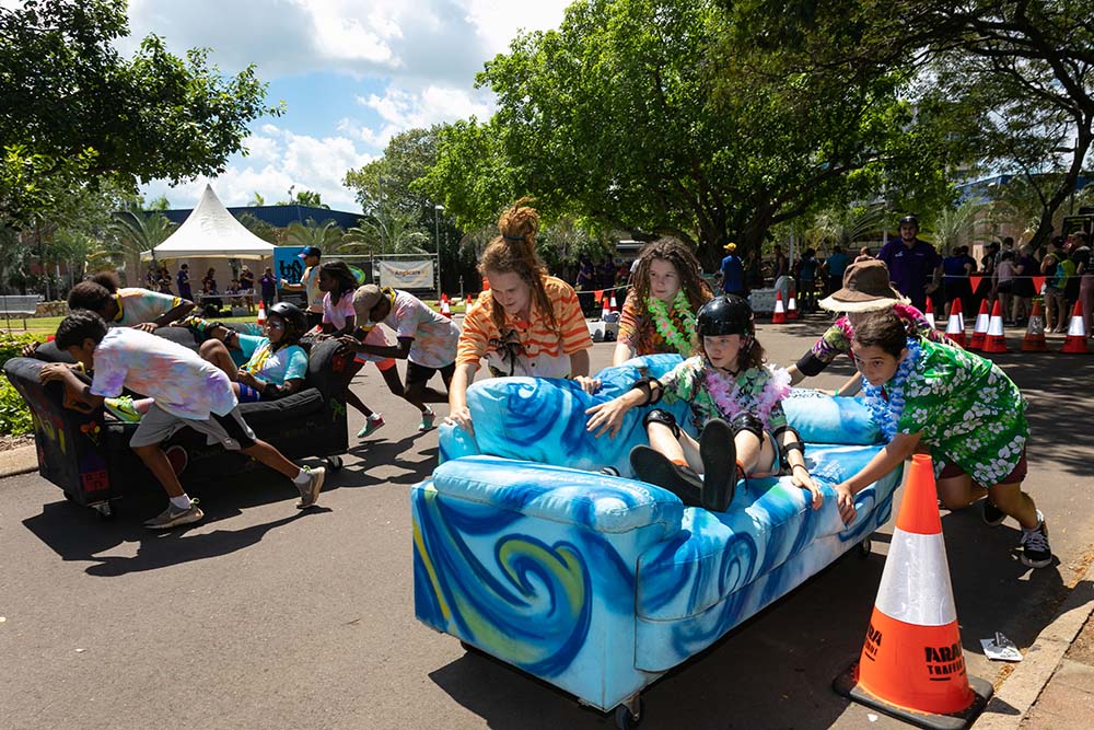 Young people racing couches at past couch surfing races. 